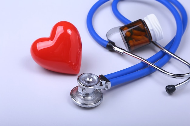 Stethoscoop, rood hart en diverse pillen op witte tafel met ruimte voor tekst.