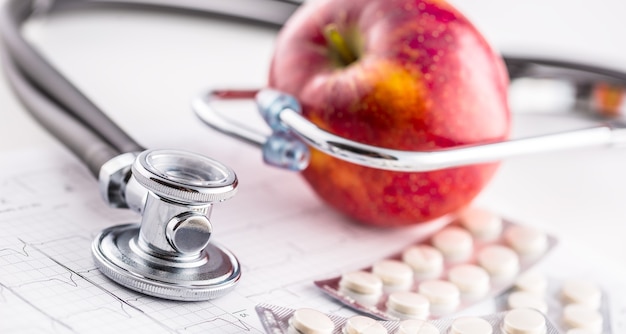 Stethoscope apple and pills on white background.