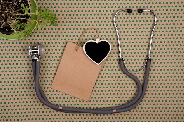 Stethoscope blank blackboard in the form of heart shopping bag gift bags and flower on craft paper background in green polka dots