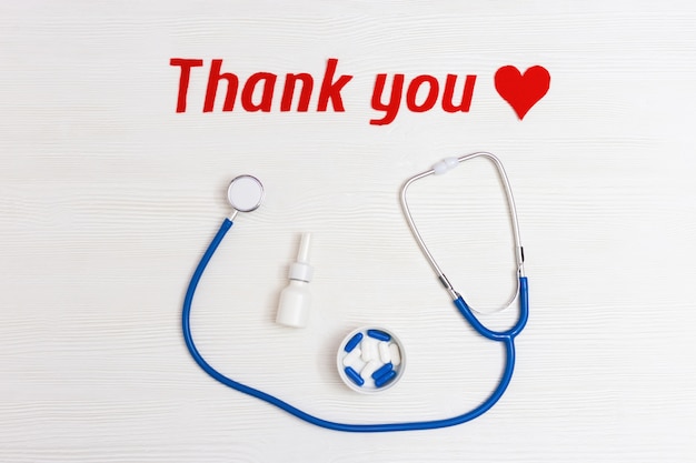 Stethoscope blue colored, pills, red heart and text "thank you" on white