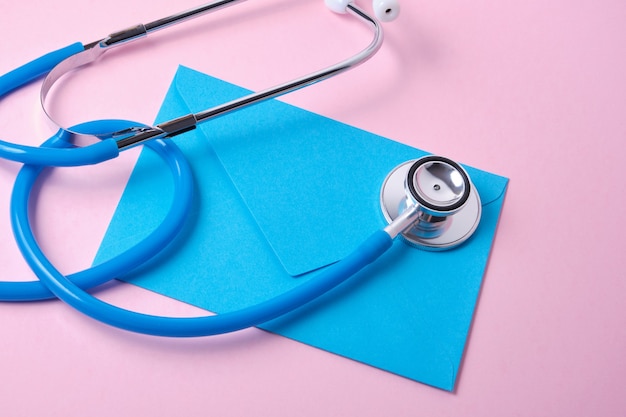 ピンクの表面の医者の日の聴診器と青い封筒