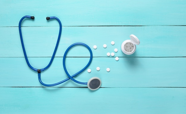 Stethoscope and bottle with pills on a blue wooden