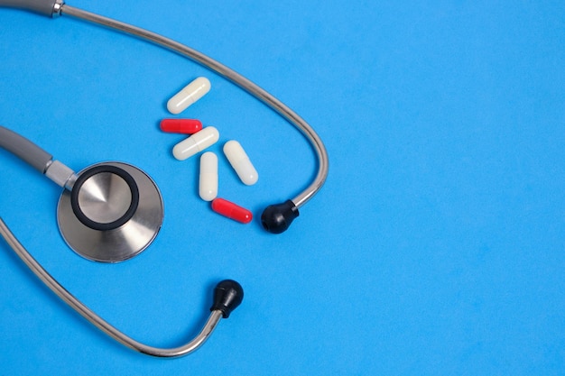 Stethoscope and bunch pills on blue background.