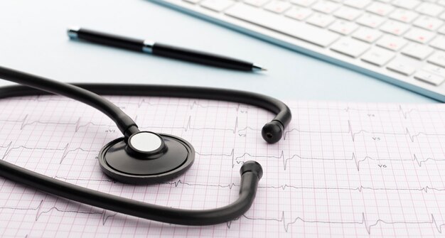 Stethoscope on cardiogram with pen and keyboard on blue background.