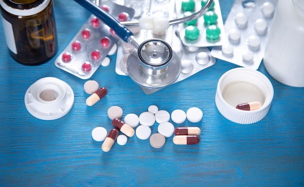 Stethoscope and different pills on the blue background.