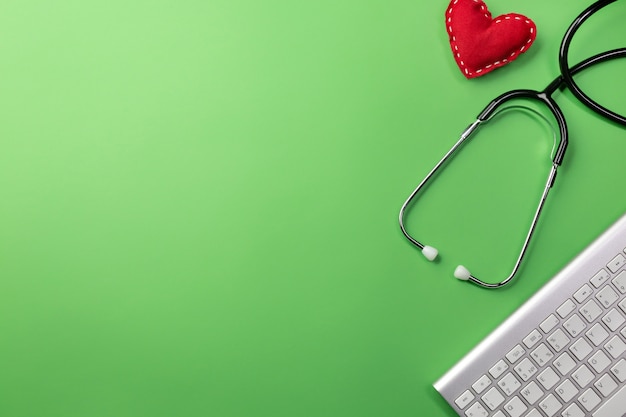 Stethoscope in doctors desk with keyboard and heart background