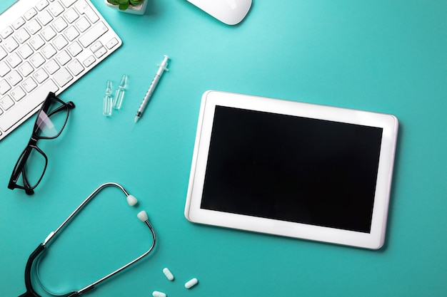 Stethoscope in doctors desk with tablet, keyboard, mouse, syringe and ampoules. Top view with place for your text.