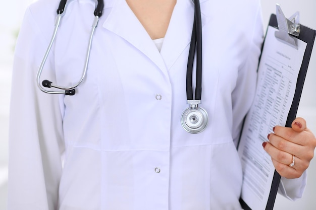 Stethoscope at female doctor breast at hospital office. Unknown physician's hands close-up. Medicine and health care concept.