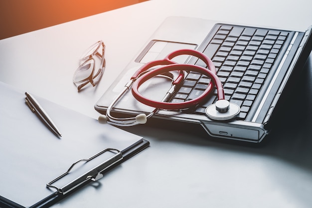 Photo stethoscope and glasses on laptop with clipboard blank paper