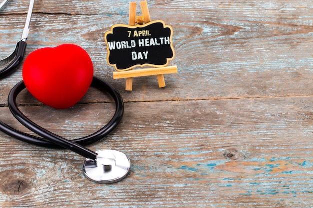 Stethoscope and heart symbol with inscription World Health Day on wooden background with copy space.