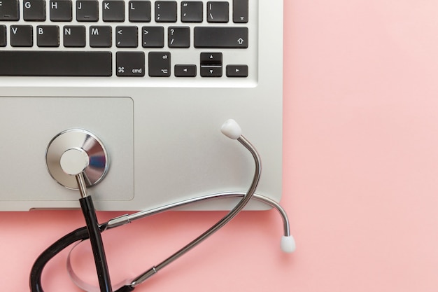 Stethoscope keyboard laptop computer isolated on pink background. Modern medical Information technology and sofware advances concept. Computer and gadget diagnostics and repair. Flat lay top view