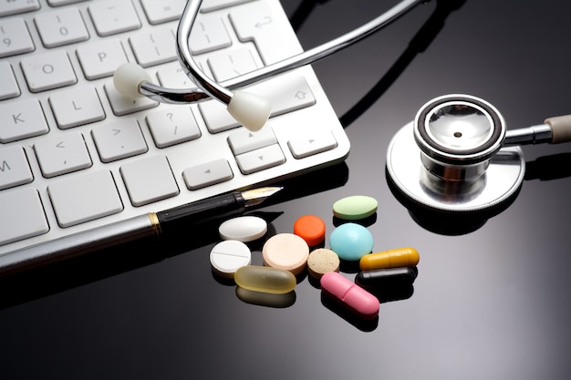 Stethoscope, keyboard and pills on black background