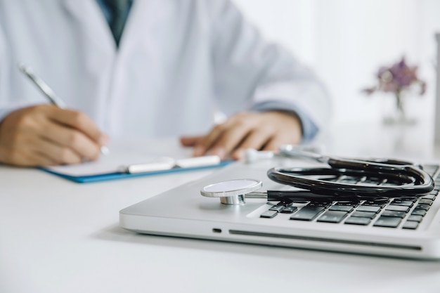 Stethoscope and Laptop on desk,Doctor working in hospital writing a prescription