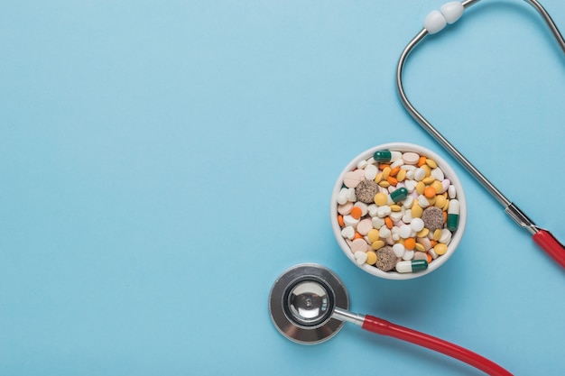 A stethoscope and a large number of tablets on a blue background. Space for the text. Flat lay.