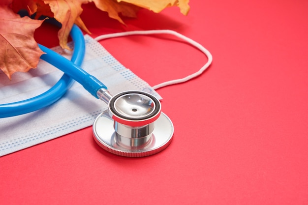 Stethoscope and leaves on red background