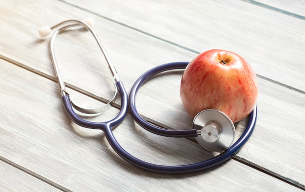 The stethoscope lies near the apple on a wooden background