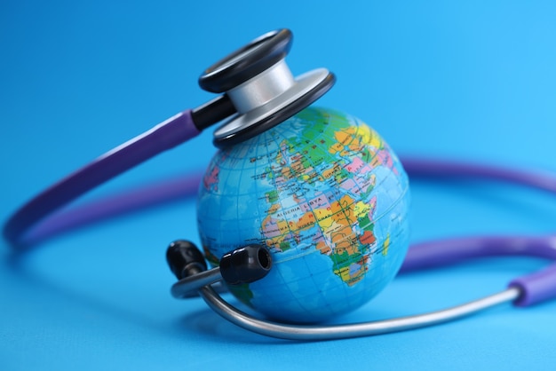 Stethoscope lying around globe on blue background. Pandemic covid-19 concept