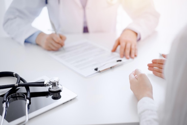 Stethoscope lying on the tablet computer in front of a doctor and patient sitting opposite each other at the background . Medicine, healthcare concept.