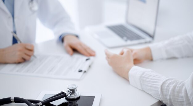 Stethoscope lying on the tablet computer in front of a doctor and patient sitting opposite each other at the background . Medicine, healthcare concept