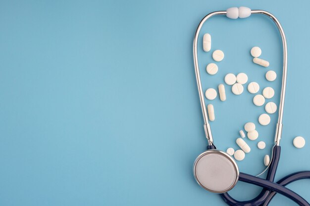 Stethoscope and many pills on blue background with copy space