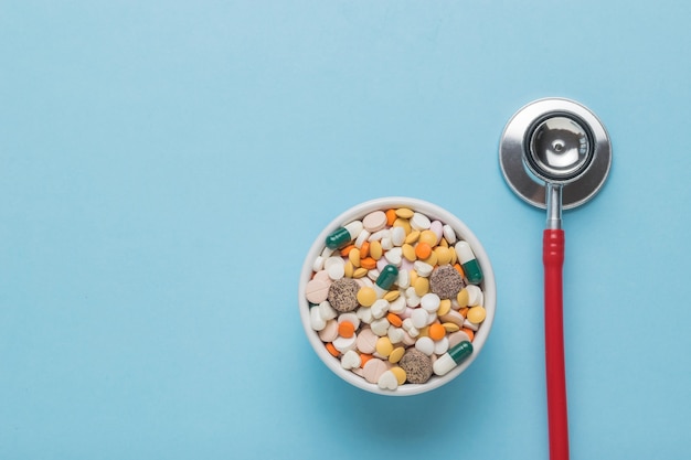 A stethoscope and medical preparations for the treatment of various diseases on a blue background. Space for the text. Flat lay.