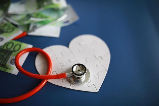 A stethoscope on money and a puzzle heart Health insurance Healthcare and medicine How much is the treatment Money and medicine World Heart Day World Health Day How much does a donor heart cost