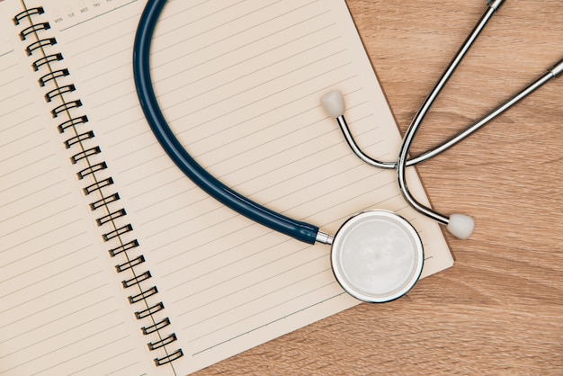 Stethoscope and notebook on wood table top view with copy space. health concept. vintage tone.