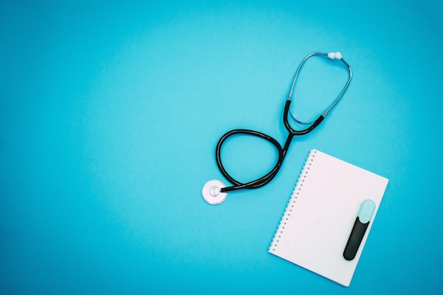Foto stetoscopio, blocco note e pennarello su sfondo azzurro. flat-lay, vista dall'alto con posto per il testo. tendenze mediche e concetto.