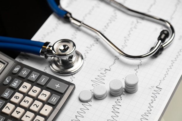 Stethoscope, pills and calculator are on a sheet with an electrocardiogram