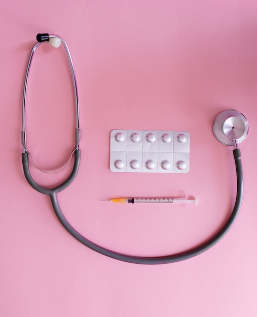 Photo stethoscope, pills and syringe on pink background for coronavirus prevention.