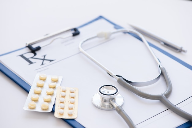 Stethoscope, prescription clipboard and bottle of pills on white surface with copy space. Health care and medical concept.