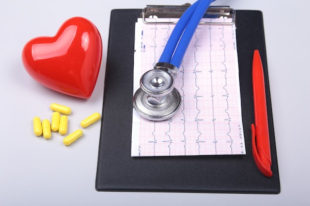 Photo stethoscope, red heart, rx prescription and assorted pills on white table with space for text.