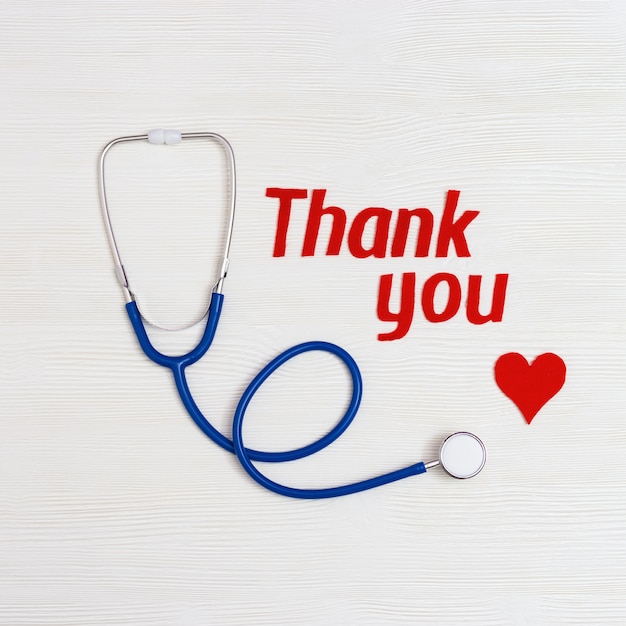 Stethoscope, red heart and text "thank you" on white wooden surface