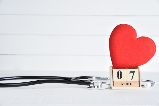 Stethoscope and Red heart with April 7 text wooden block calendar on white wooden background.