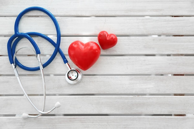 Stethoscope and red hearts on wooden background