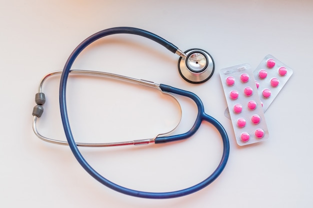 Stethoscope and some pink pills, medicine on a white background