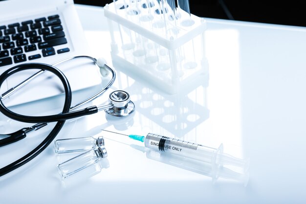 stethoscope syringe vials and laptop on a white table