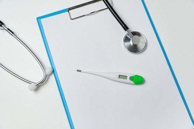 Photo stethoscope, thermometer and blank sheets of paper on white background.