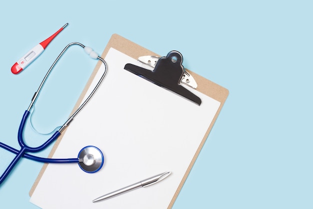A stethoscope and a thermometer on a clipboard with white sheets in a top view