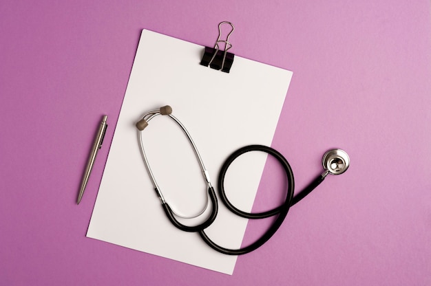 stethoscope on top of notepad with silver pen, lilac background