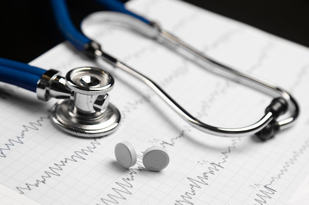 Photo stethoscope and two tablets on edge lie on a sheet with an electrocardiogram