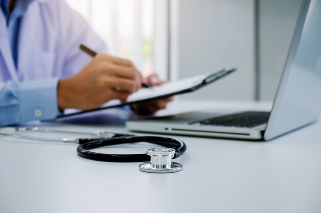 Foto stetoscopio con appunti e computer portatile sulla scrivania, medico che lavora in ospedale scrivere una prescrizione, sanità e concetto medico, risultati di test in background, colore vintage, messa a fuoco selettiva.