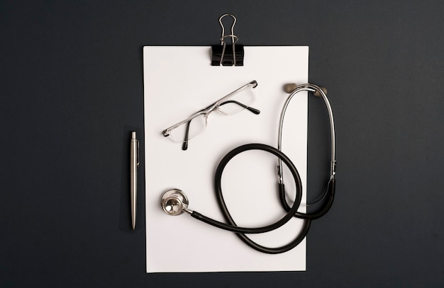 Stethoscope  with notepad, eyeglasses and silver pen, black background