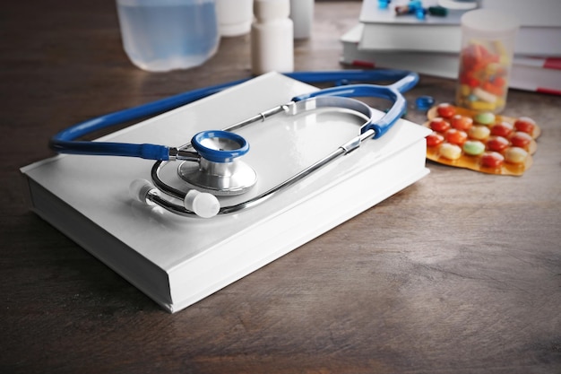 Stethoscope with open book and pills on wooden background Medical literature concept