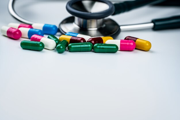 Stethoscope with pile of antibiotic capsule pills on white background