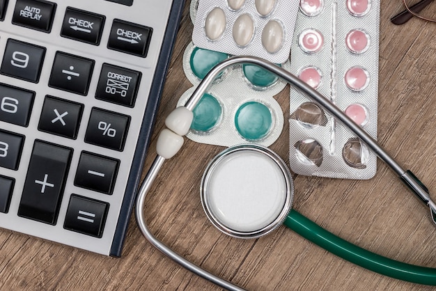 Stethoscope with pills and calculator on wooden table