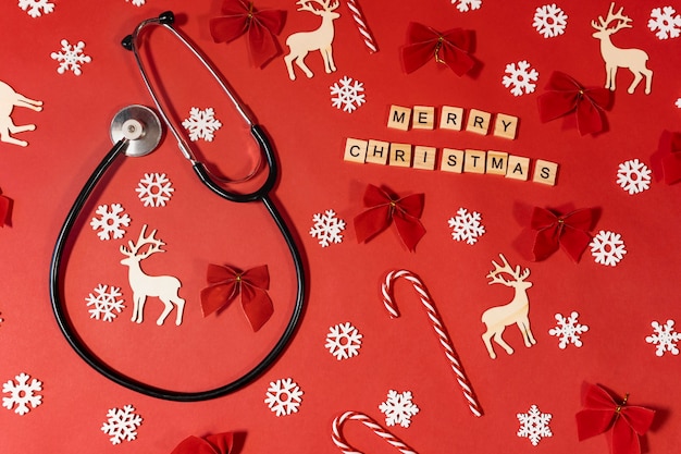 赤い背景にサンタの帽子をかぶった聴診器とお祝いの碑文メリークリスマス。クリスマス診療所のコンセプト