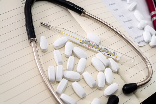 Stethoscope with a scattered pill pen on a notebook standing on a black background. Medicine concept