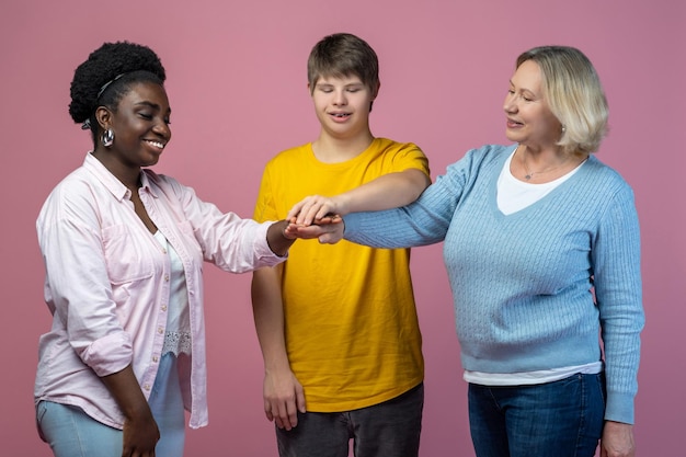 Steun. Glimlachend twee vrouwen en man met het syndroom van down staan met uitgestrekte armen aanraken met handpalmen op lichte achtergrond