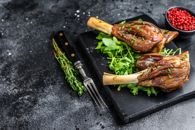 Stinco di agnello in umido su una tavola di marmo con rucola. sfondo nero. vista dall'alto. copia spazio.